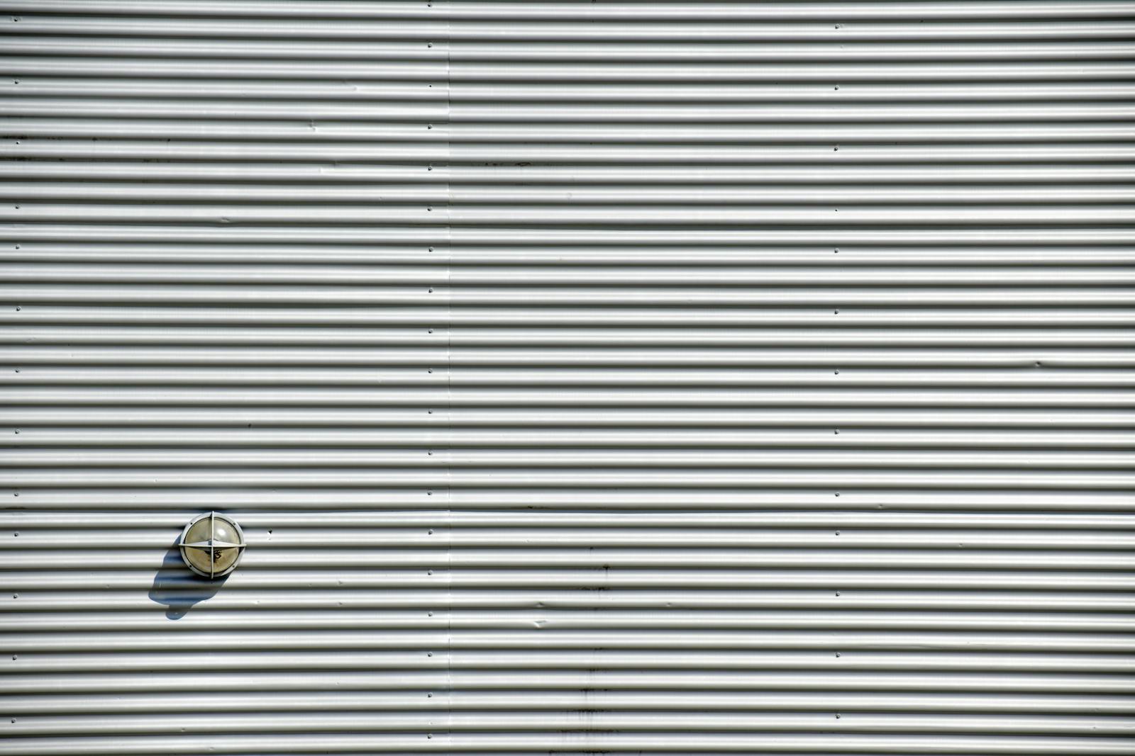 Corrugated metal wall featuring a round light fixture casting a shadow. Perfect industrial background.