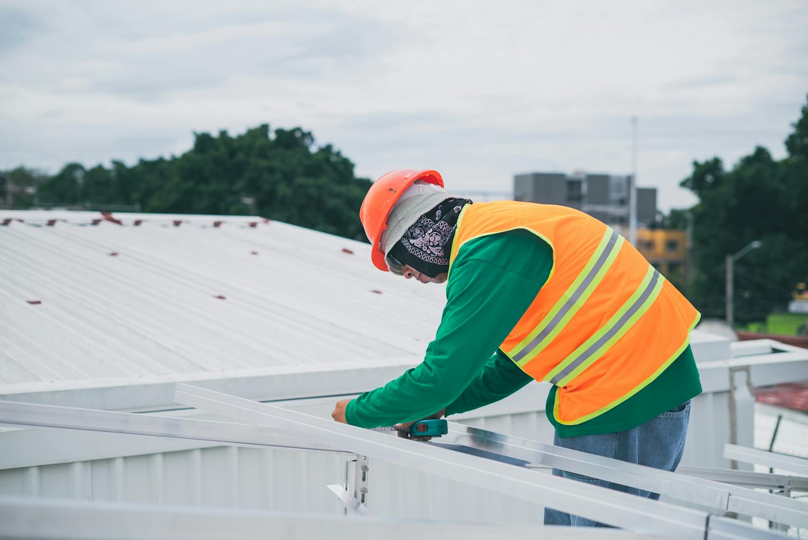 A construction worker wearing safety gear working on rooftop installation outdoors.